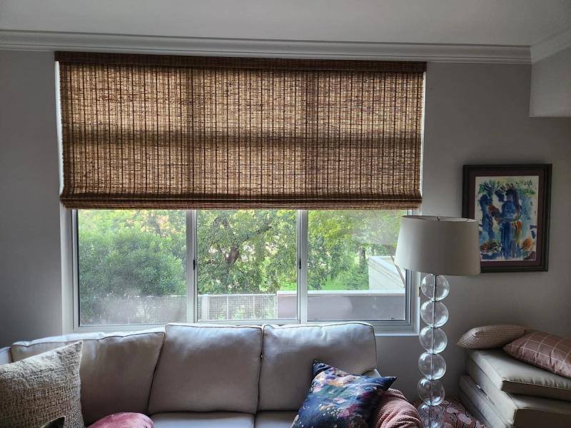 Woven bamboo Roman shade partially lowered over a wide triple-pane window in a living room
