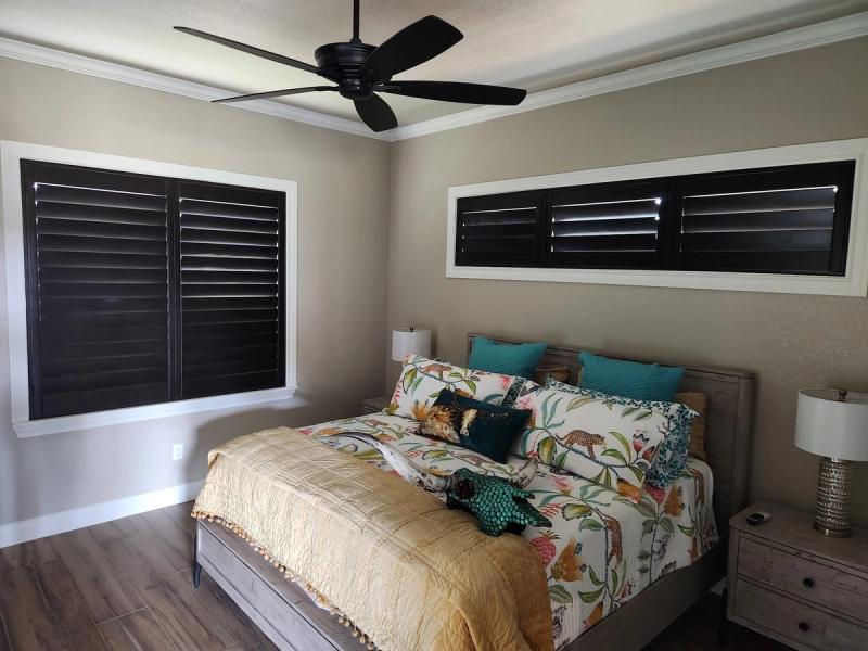 Black shutters on two bedroom windows with tropical bedding and tray ceiling