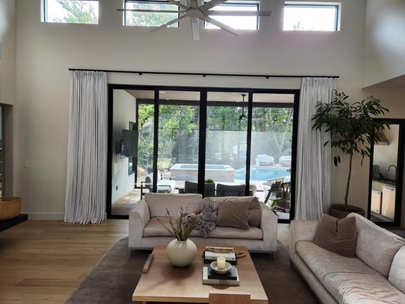 White pinch-pleat drapery panels flanking large black-framed sliding glass doors in modern living room