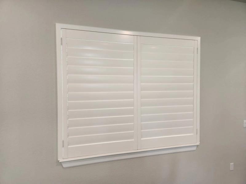 White shutters with wide louvers installed on a single window in a gray-walled room