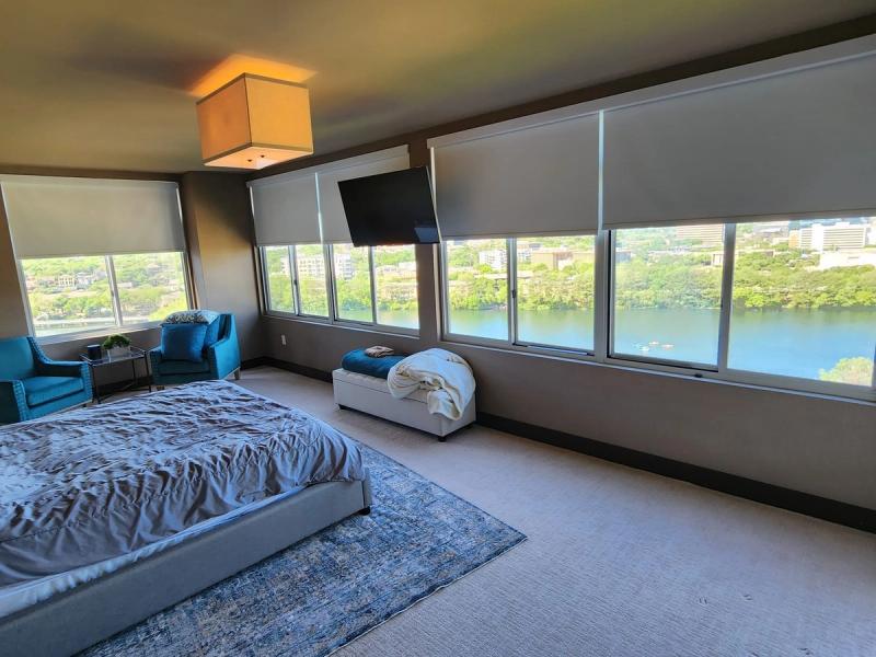 Light gray roller shades on panoramic bedroom windows overlooking a river and cityscape