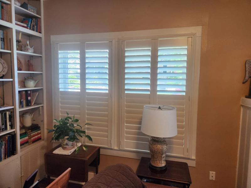 White shutters on a large window in a cozy home library with bookshelves