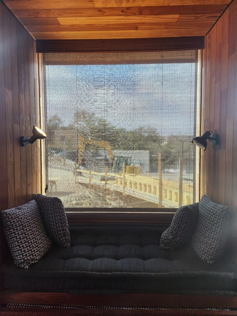 Woven solar shade on a wood-paneled window seat nook with two sconce lights