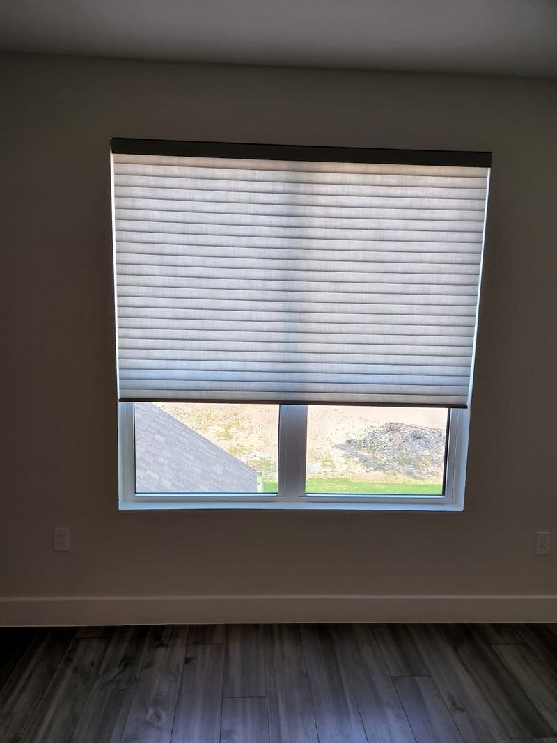 Light gray cellular honeycomb shade partially lowered on a wide double window