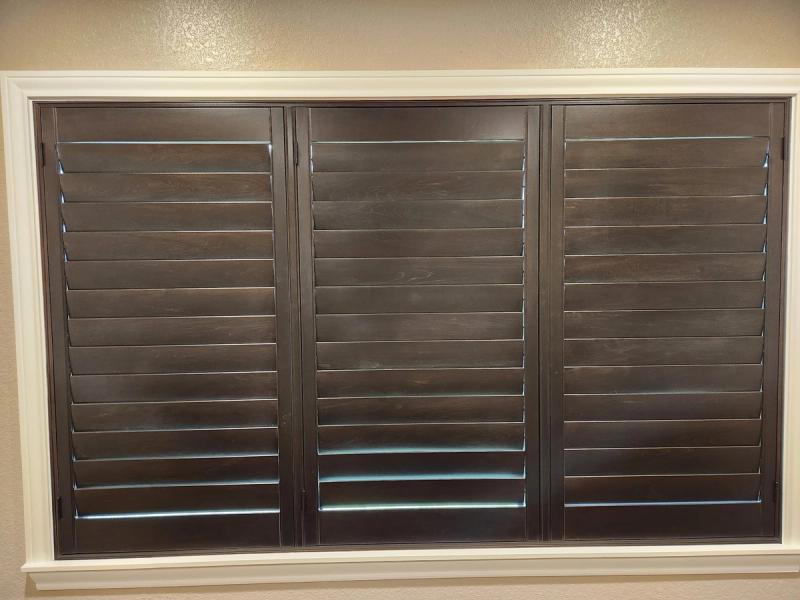 Dark espresso shutters with wide louvers installed in a wide interior window