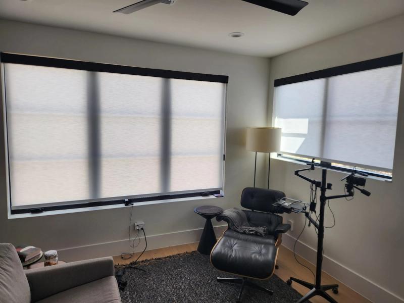 Solar roller shades on two large windows in a modern living room with Eames lounge chair