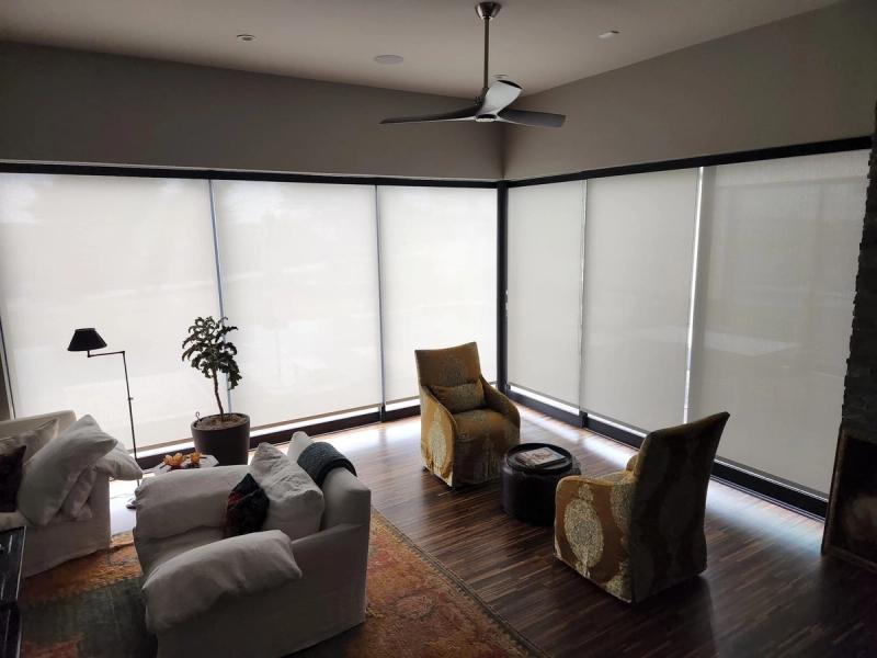 White solar roller shades covering floor-to-ceiling corner windows in a modern living room