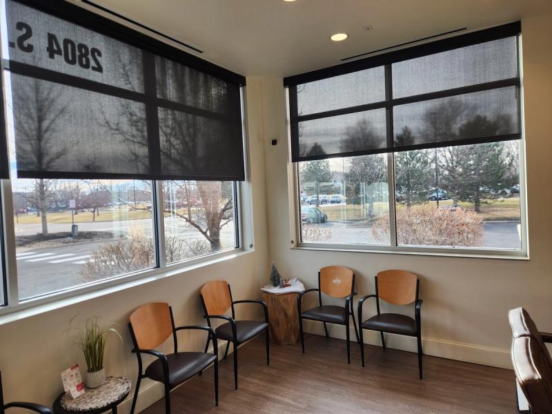 Dark solar roller shades partially lowered on large windows in a medical waiting room