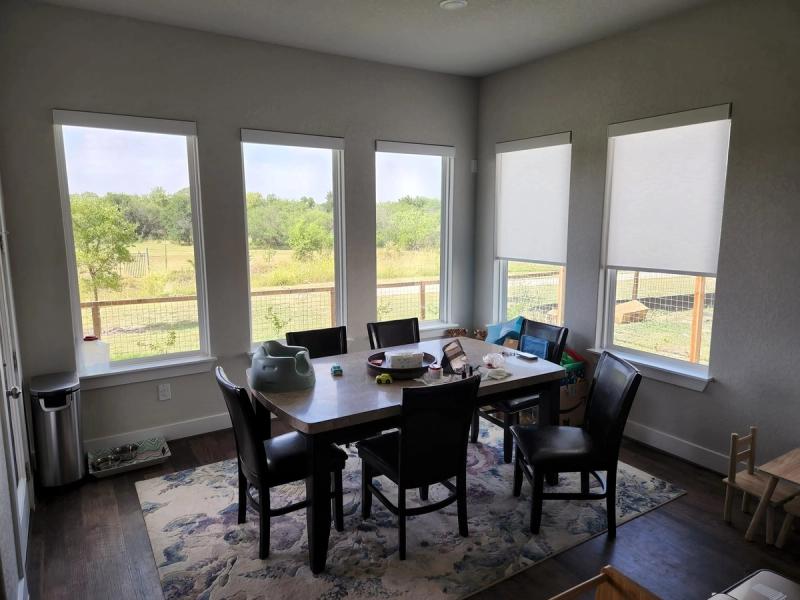 White roller shades on corner dining room windows overlooking rural field and trees