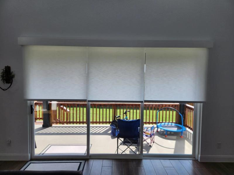 Three white roller shades partially lowered over wide sliding glass patio doors