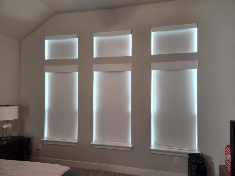 Three white roller shades with LED backlighting on tall bedroom windows at night