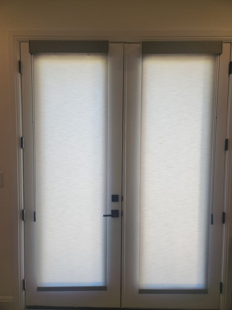 White roller shades fully lowered on double French doors with dark hardware