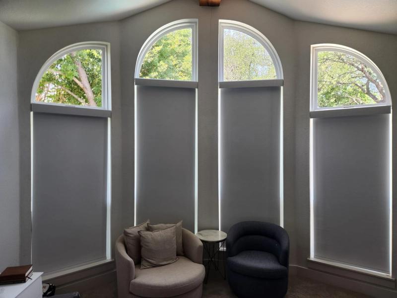 Gray roller shades on four tall arched windows in a sitting room with two chairs