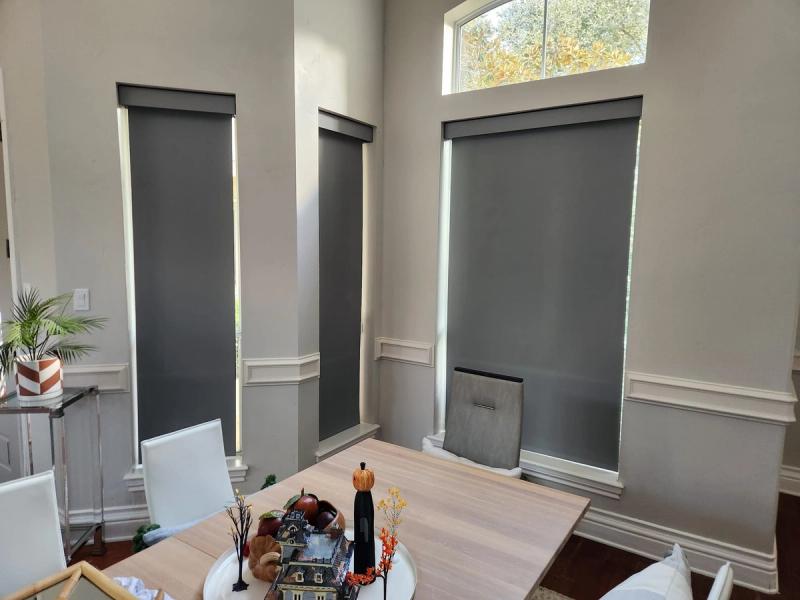 Dark gray roller shades on tall narrow windows in a dining room with wainscoting