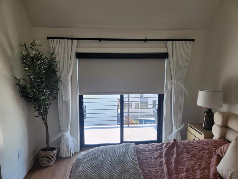 Gray roller shade and white pinch-pleat drapes on sliding glass door in bedroom