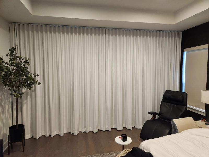 Floor-to-ceiling white ripple-fold drapery panels covering a wide bedroom wall