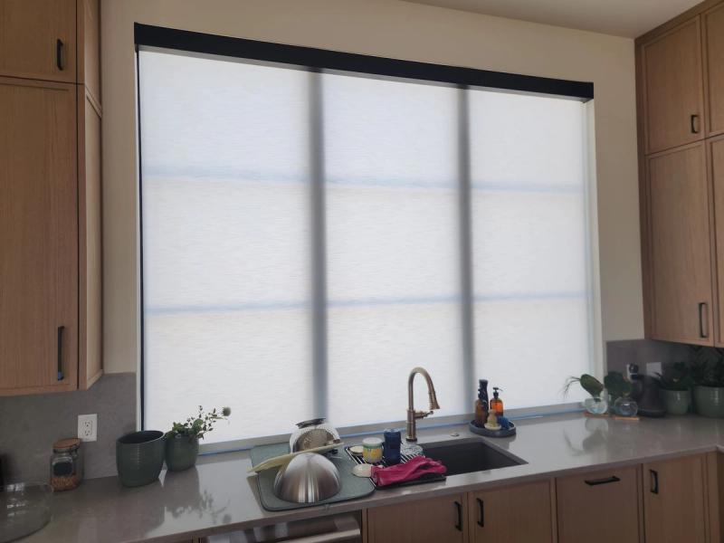 Three white solar roller shades covering a large kitchen window above a sink