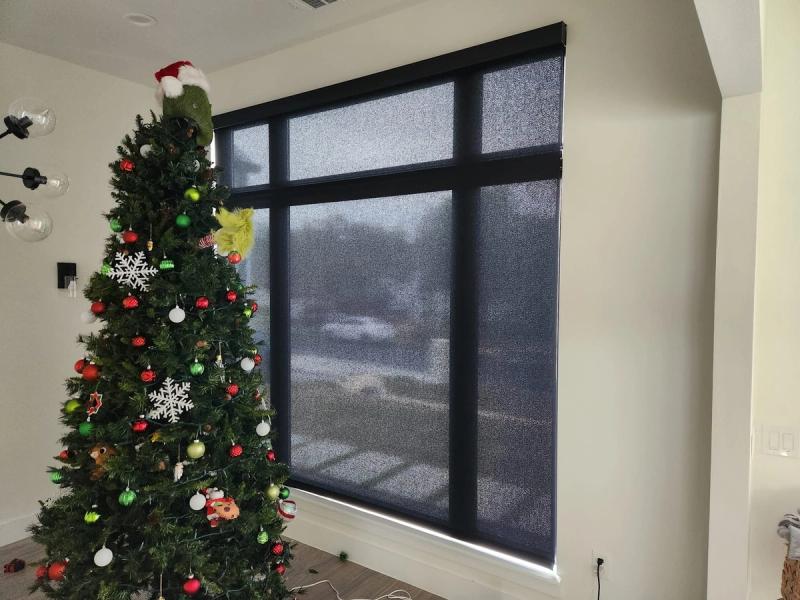 Dark solar roller shades covering large multi-panel window beside decorated Christmas tree