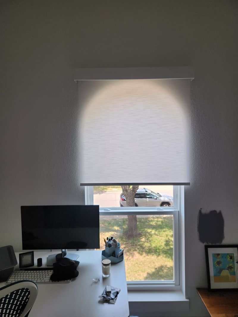 White roller shade partially lowered on a single window above a home office desk