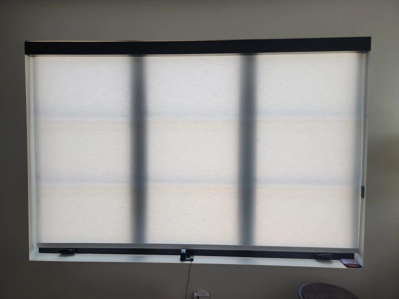 Three white solar roller shades fully lowered on a wide interior window with dark hardware