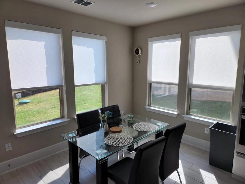White solar roller shades on four windows in a bright dining room with glass table
