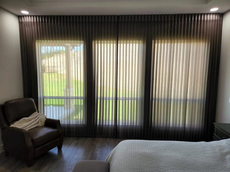 Dark brown sheer ripple-fold drapery panels covering large sliding glass doors in a bedroom