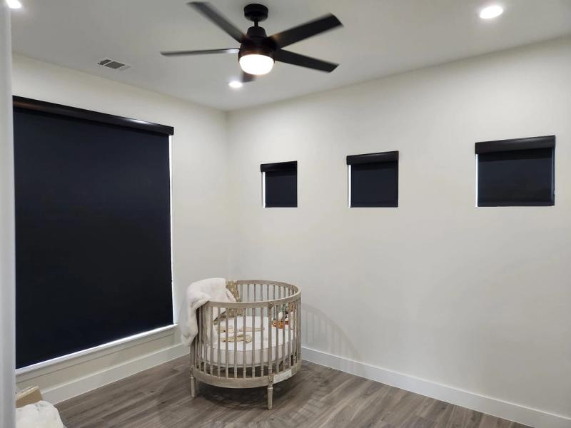 Blackout roller shades on multiple windows in a modern nursery with round crib