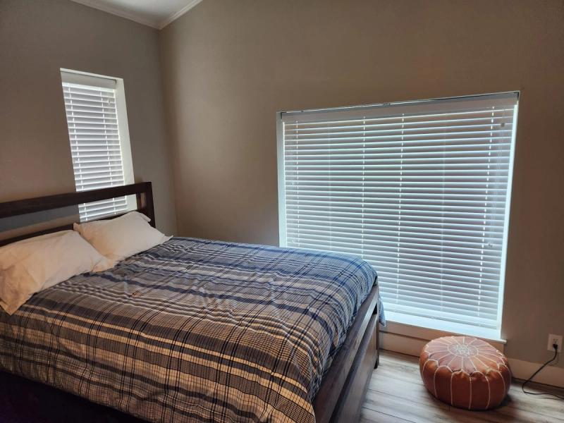White horizontal blinds on two bedroom windows beside a bed with plaid bedding