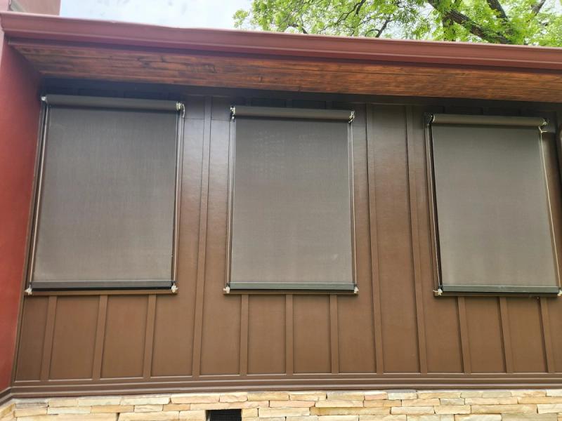 Three dark gray exterior roller shades mounted on brown metal panel outdoor wall