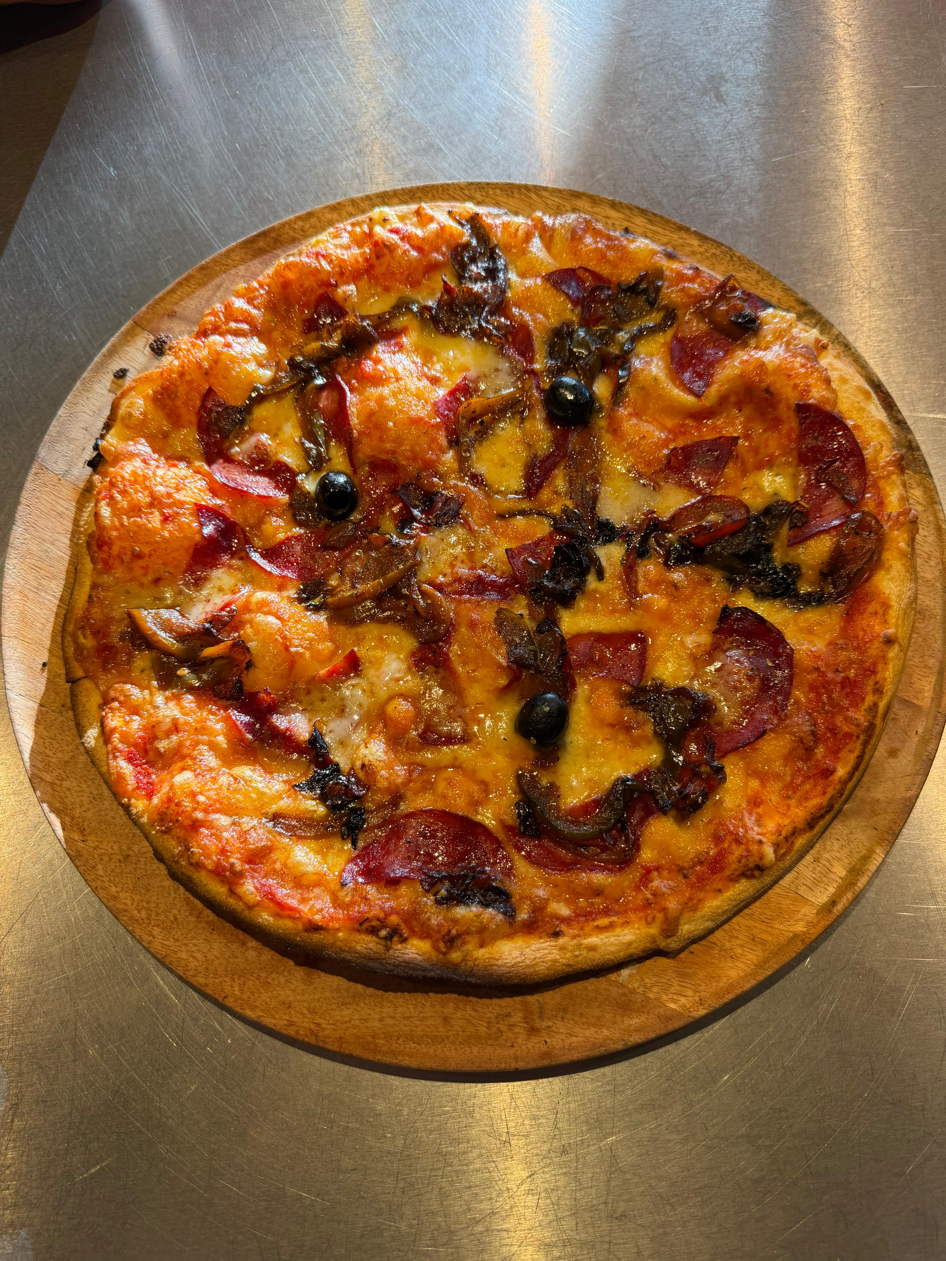 Pizza Chorizo artisanale garnie de rondelles de chorizo, poivrons, fromage fondu et olives noires, présentée sur une planche en bois à la pizzeria Chez Matteo au Porge.
