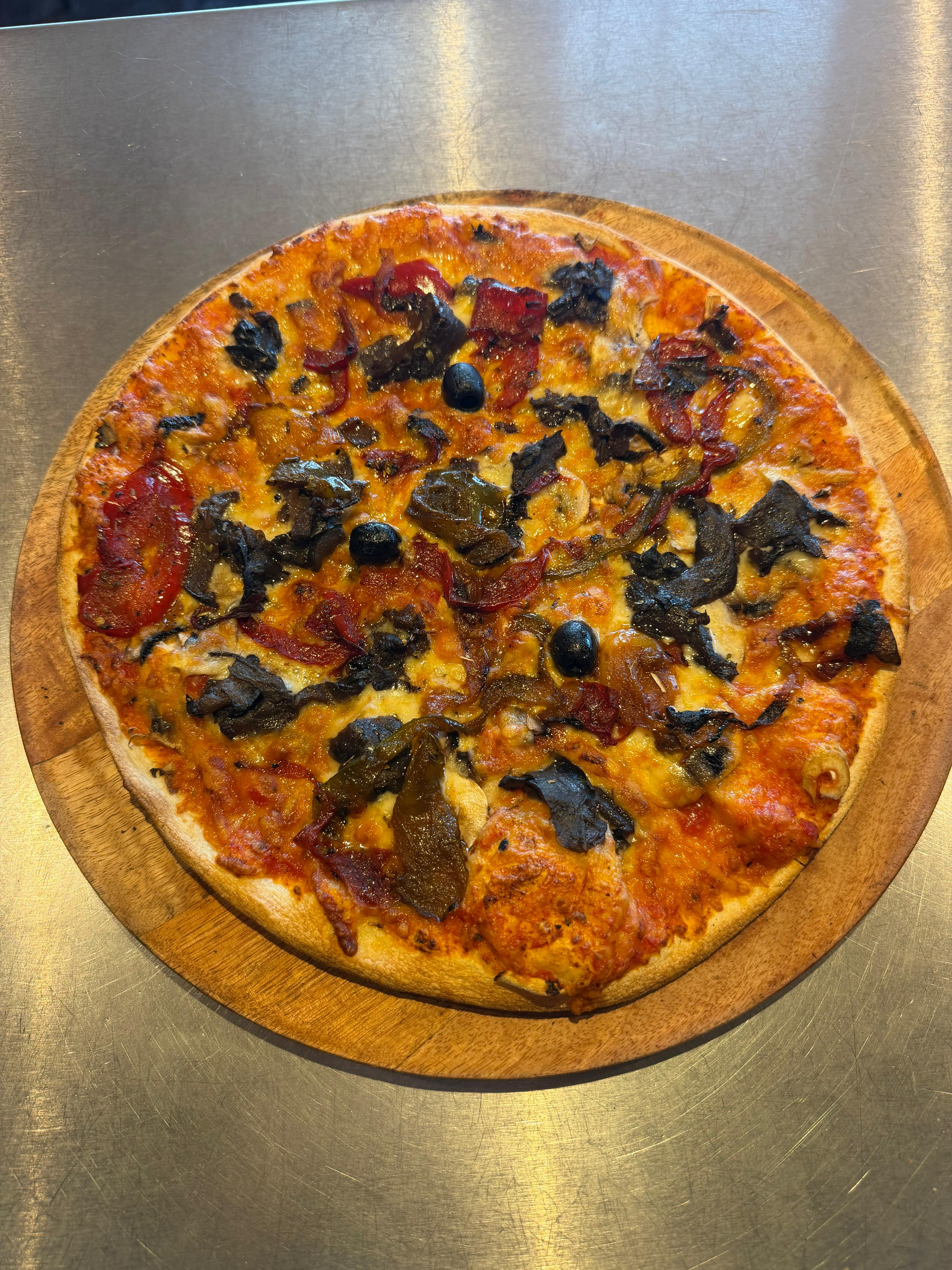 Pizza Végétarienne artisanale garnie de champignons, poivrons, aubergines grillées, fromage fondu et olives noires, présentée sur une planche en bois à la pizzeria Chez Matteo au Porge.