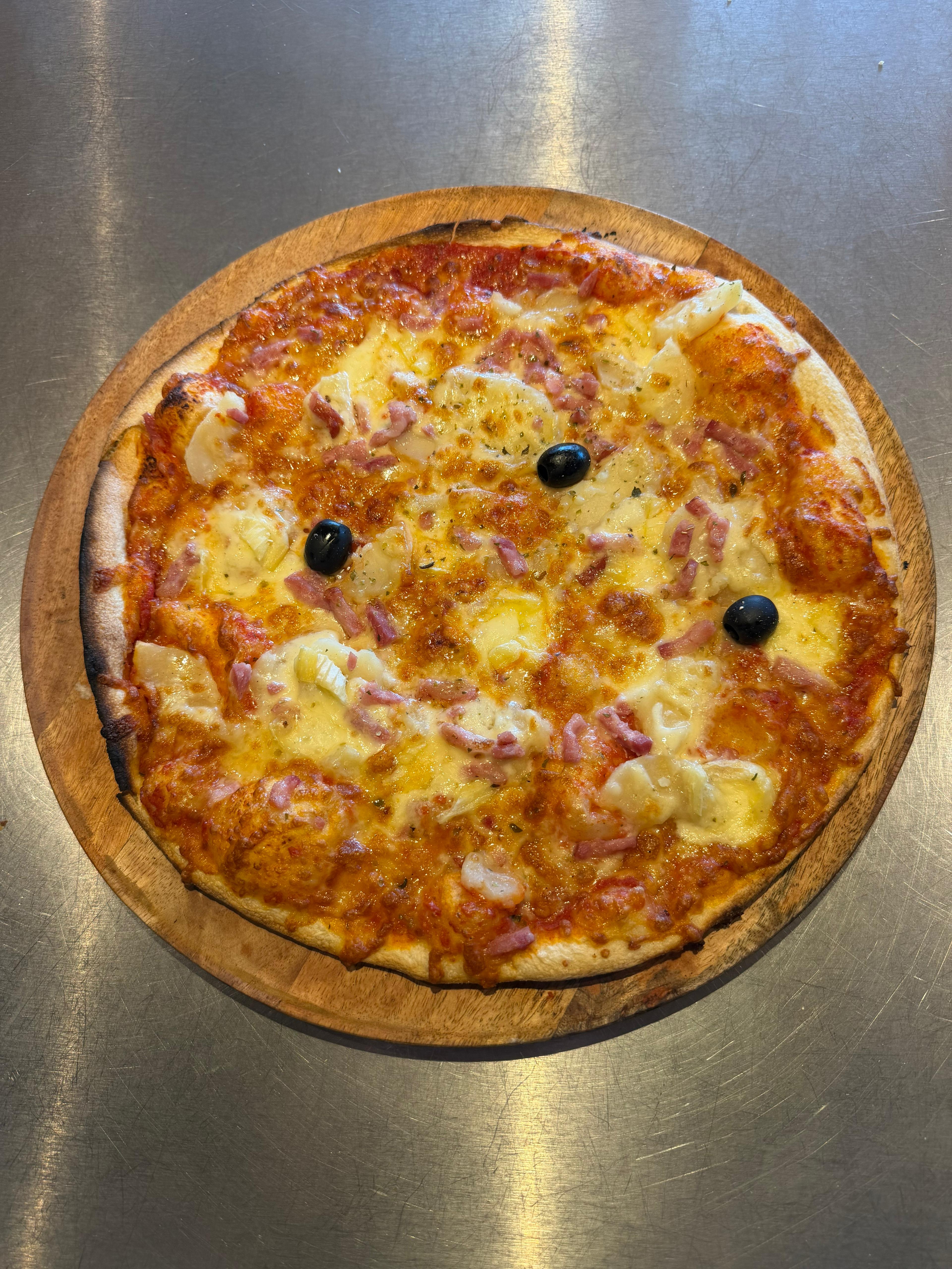 Pizza Reblochon artisanale garnie de pommes de terre, lardons, fromage fondu et olives noires, présentée sur une planche en bois à la pizzeria Chez Matteo au Porge.