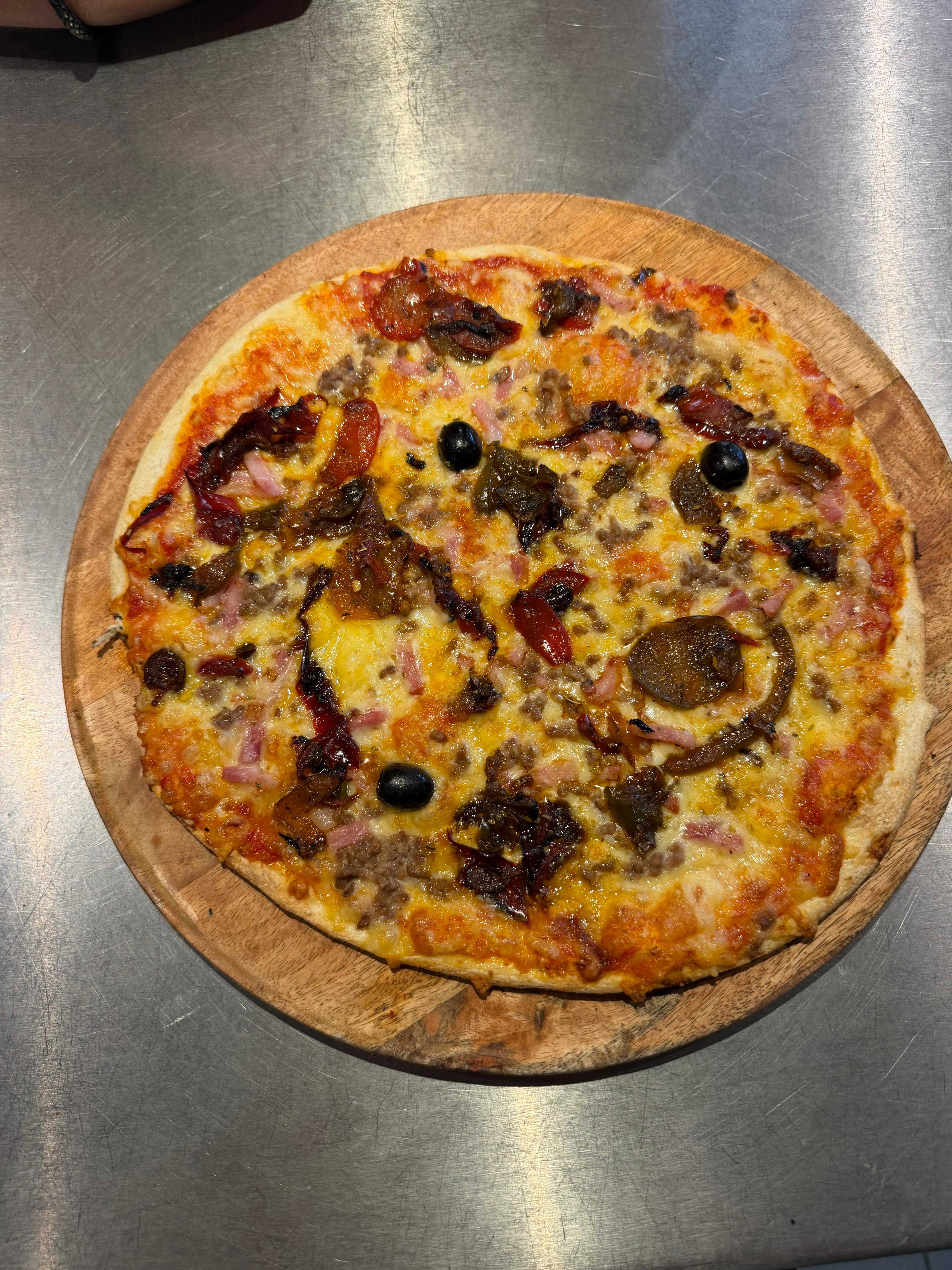Pizza Country artisanale garnie de viande hachée, poivrons, lardons, fromage fondu et olives noires, présentée sur une planche en bois à la pizzeria Chez Matteo au Porge.
