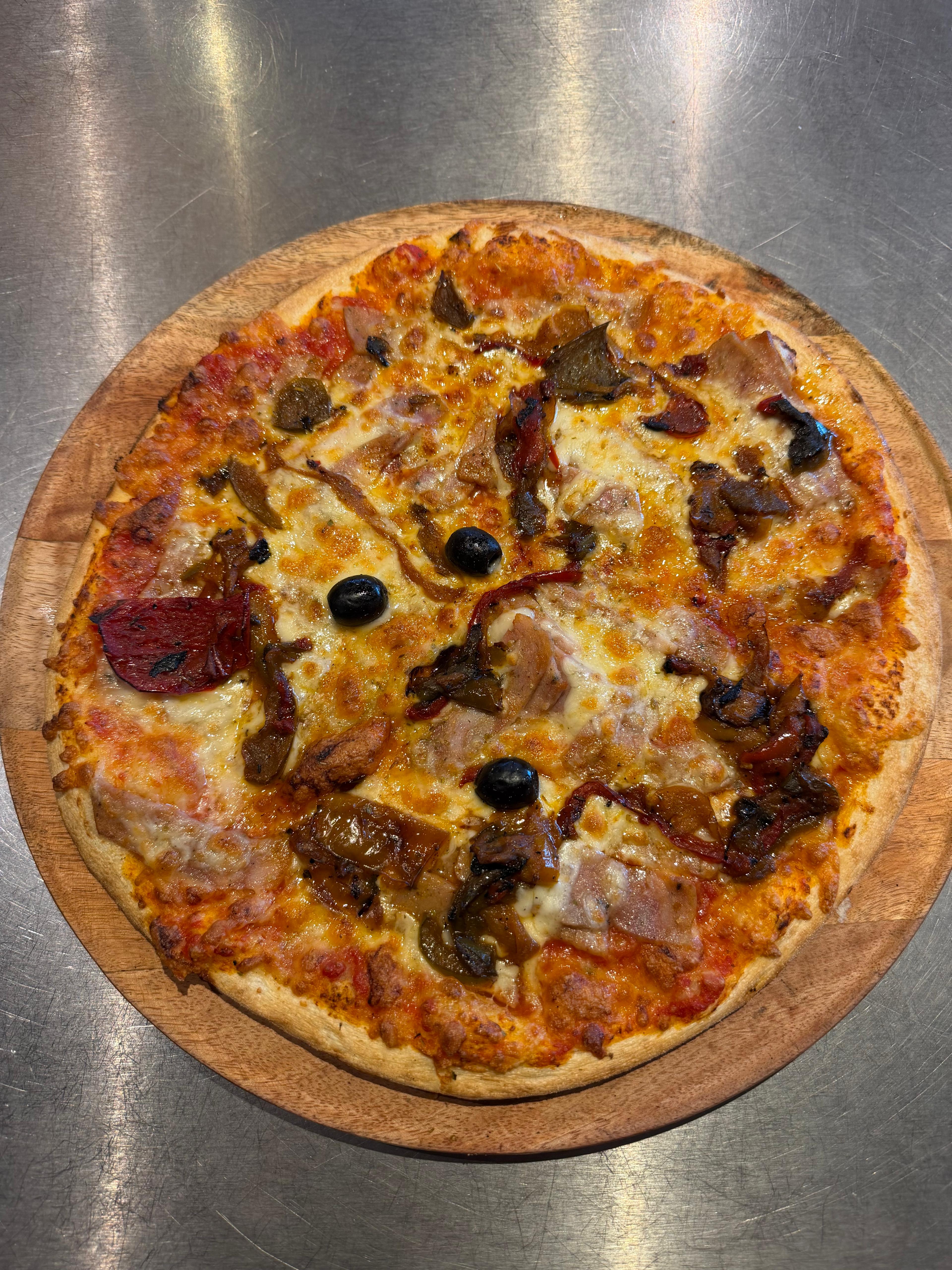 Pizza Melting-Pot artisanale garnie de merguez, chorizo, lardons, poivrons, fromage fondu et olives noires, présentée sur une planche en bois à la pizzeria Chez Matteo au Porge.