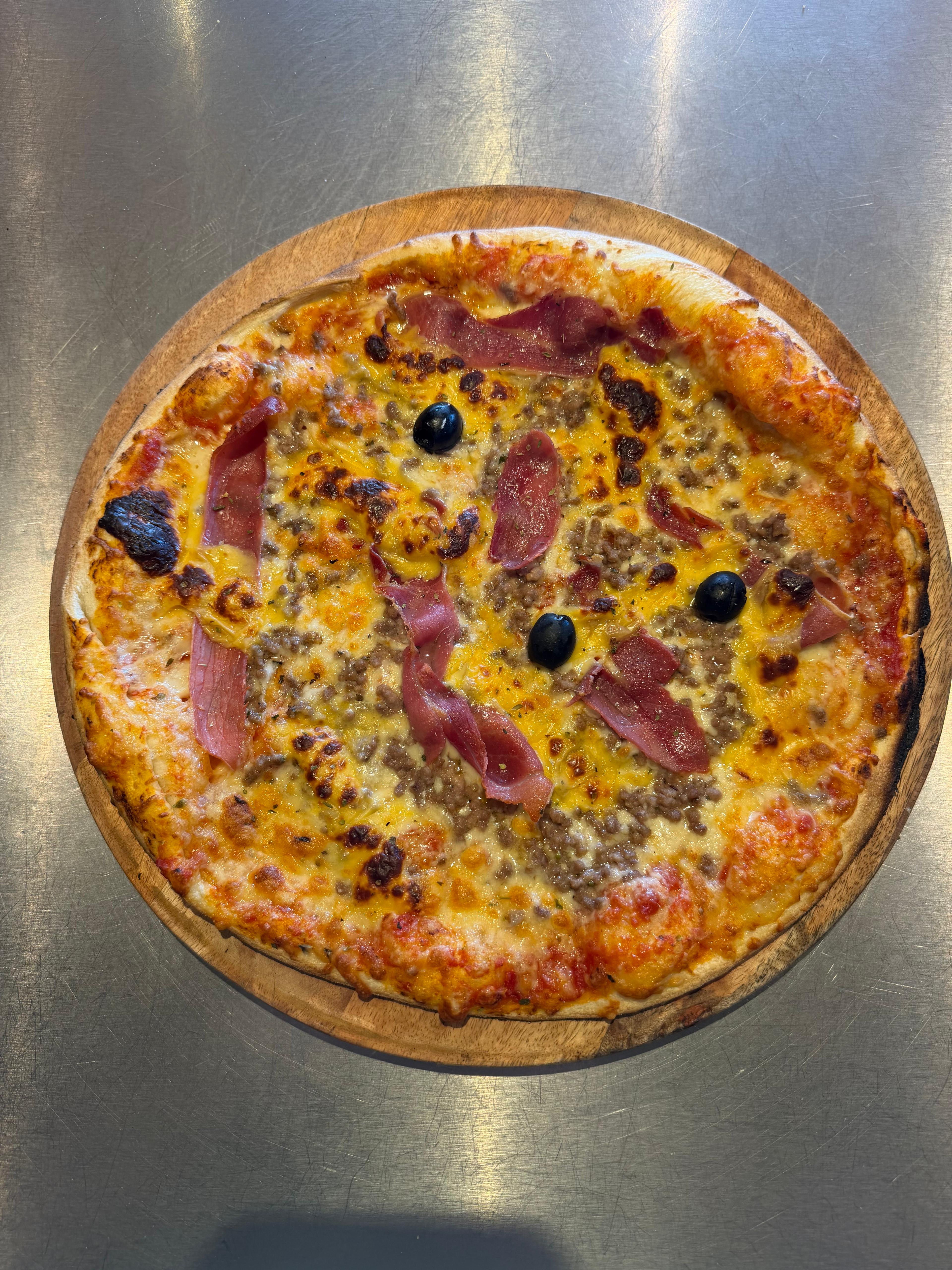 Pizza Burgers artisanale garnie de viande hachée, cheddar, jambon de pays, fromage fondu et olives noires, présentée sur une planche en bois à la pizzeria Chez Matteo au Porge.