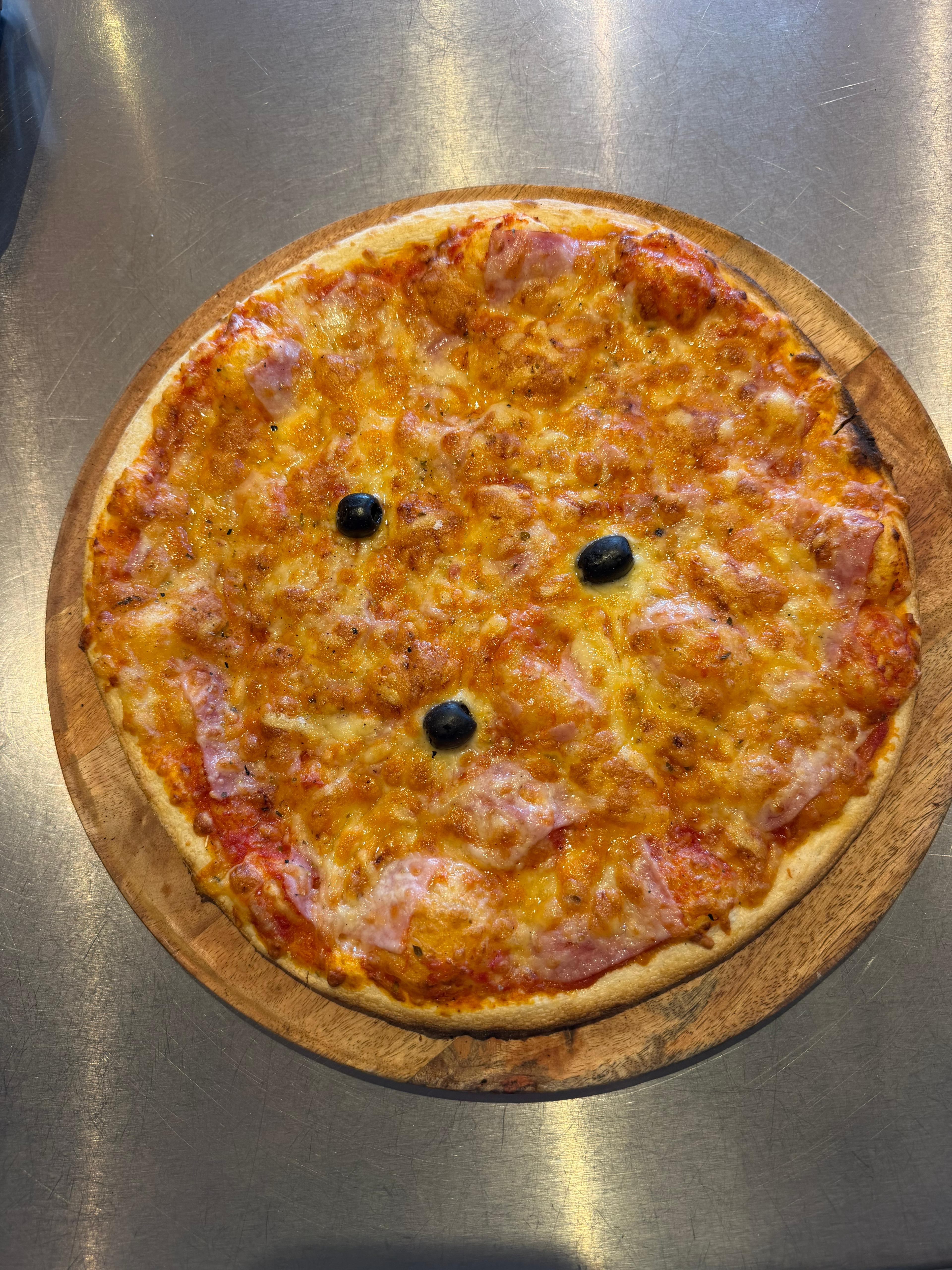 Pizza Reine classique et généreuse, garnie de tranches de jambon blanc, d'un savoureux mélange d'emmental et de mozzarella fondus, décorée de quelques olives noires.