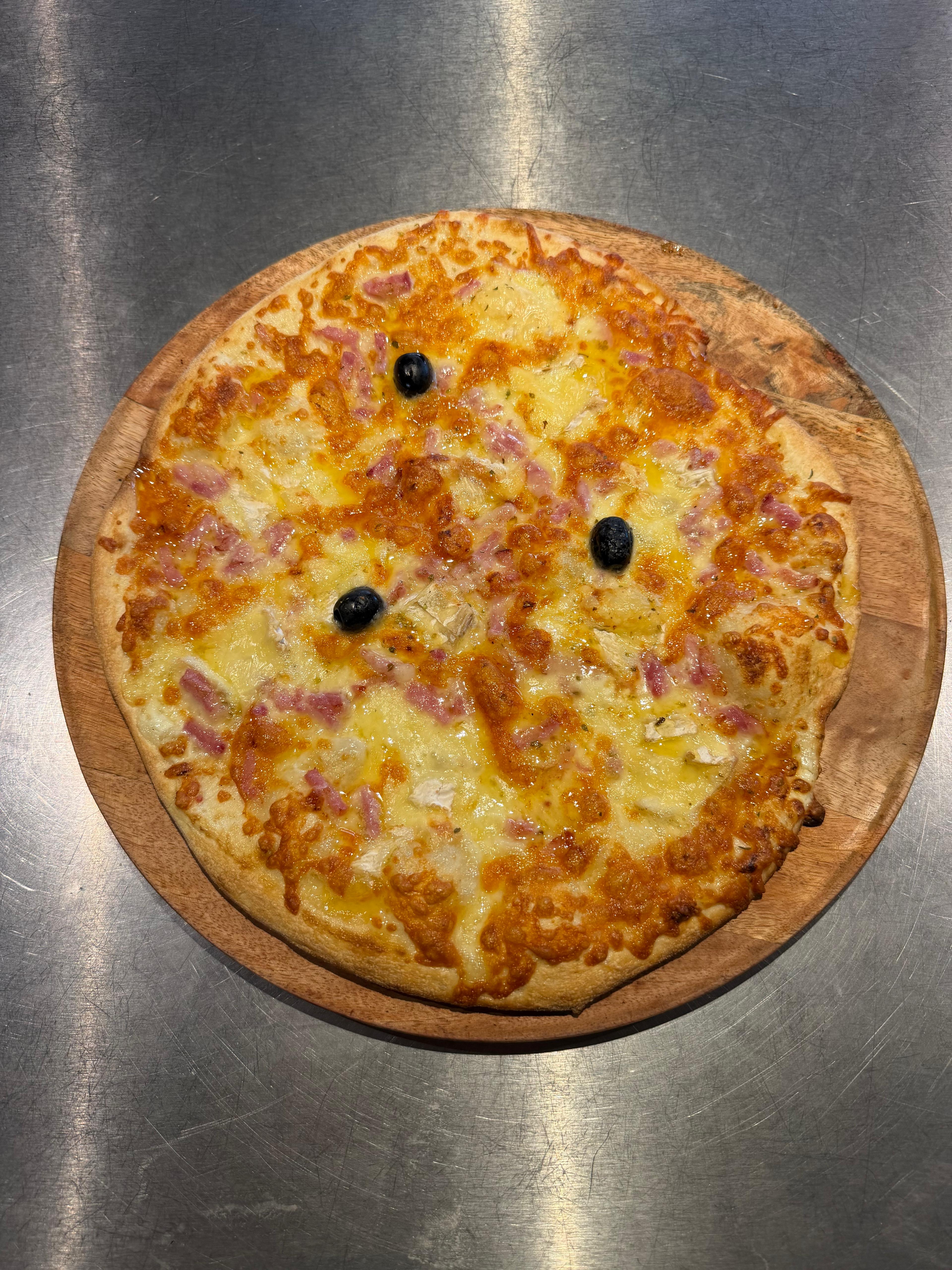 Pizza Biquette artisanale garnie de lardons, morceaux de chèvre, filet de miel, fromage fondu et olives noires, présentée sur une planche en bois à la pizzeria Chez Matteo au Porge.