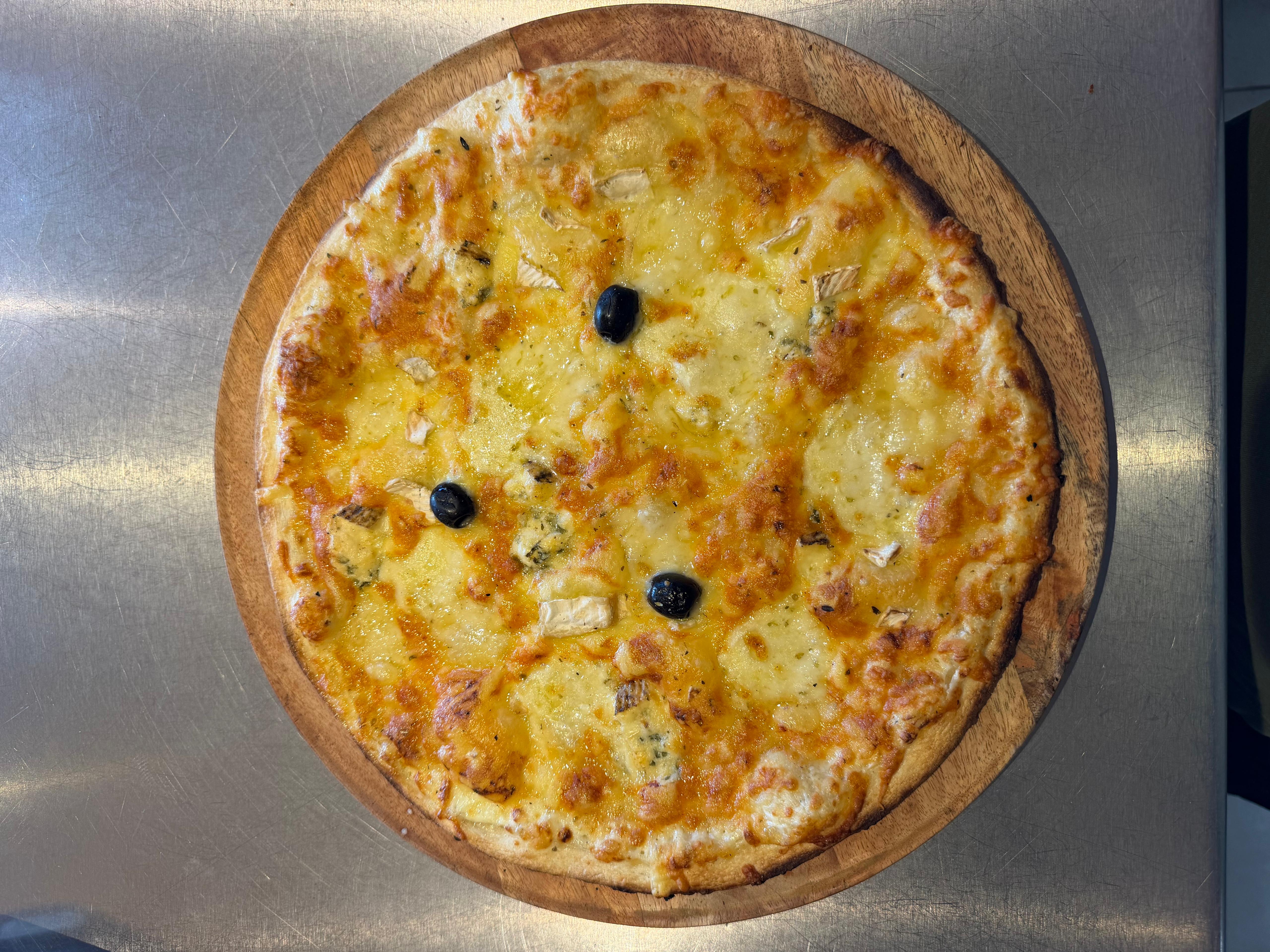 Pizza aux 5 fromages artisanale, richement garnie de comté, mozzarella fraîche, bleu, camembert, emmental et olives noires, présentée sur une planche en bois à la pizzeria Chez Matteo au Porge.
