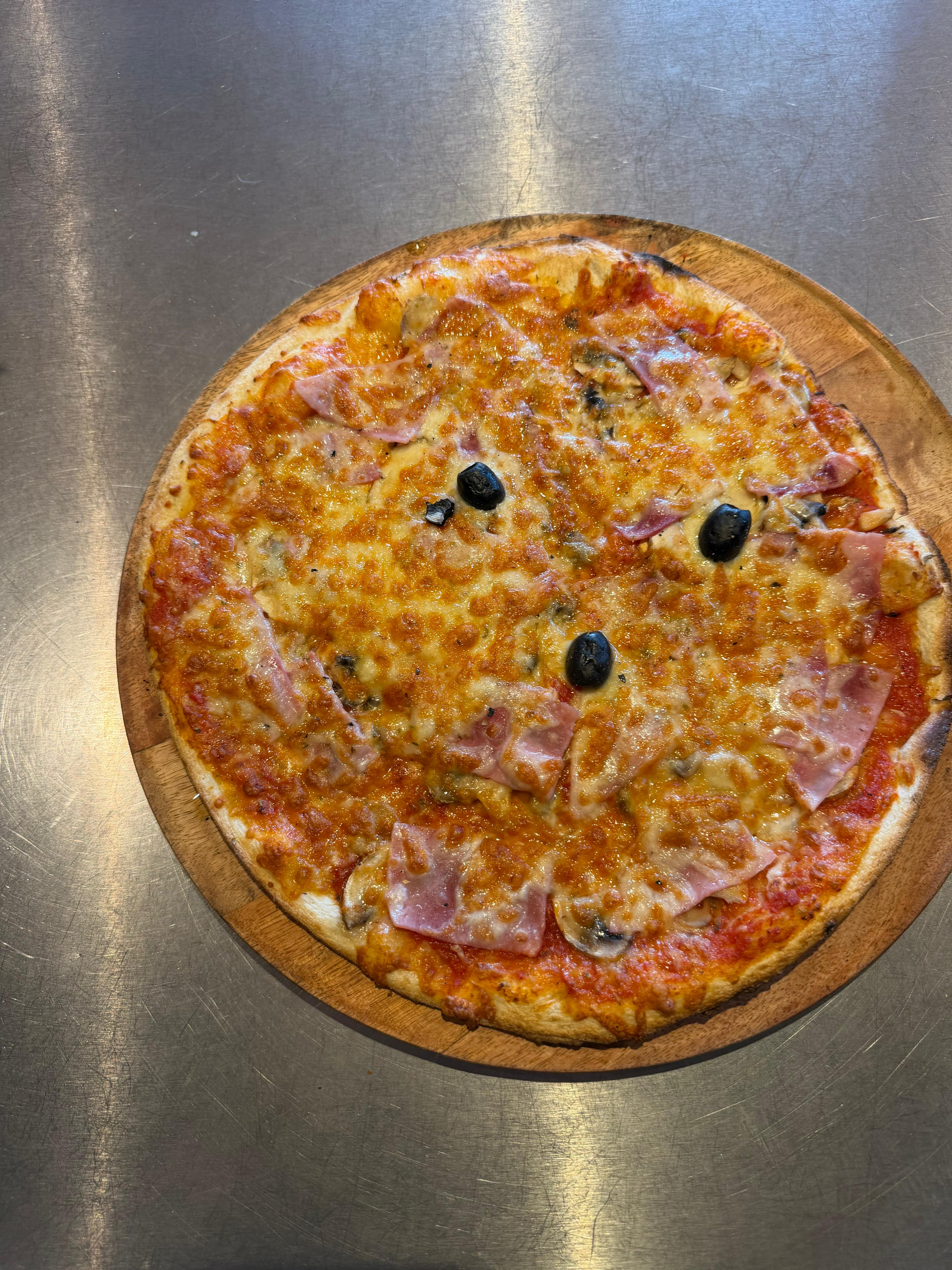 Pizza Regina artisanale garnie de jambon blanc, champignons, fromage fondu et olives noires, présentée sur une planche en bois à la pizzeria Chez Matteo au Porge.