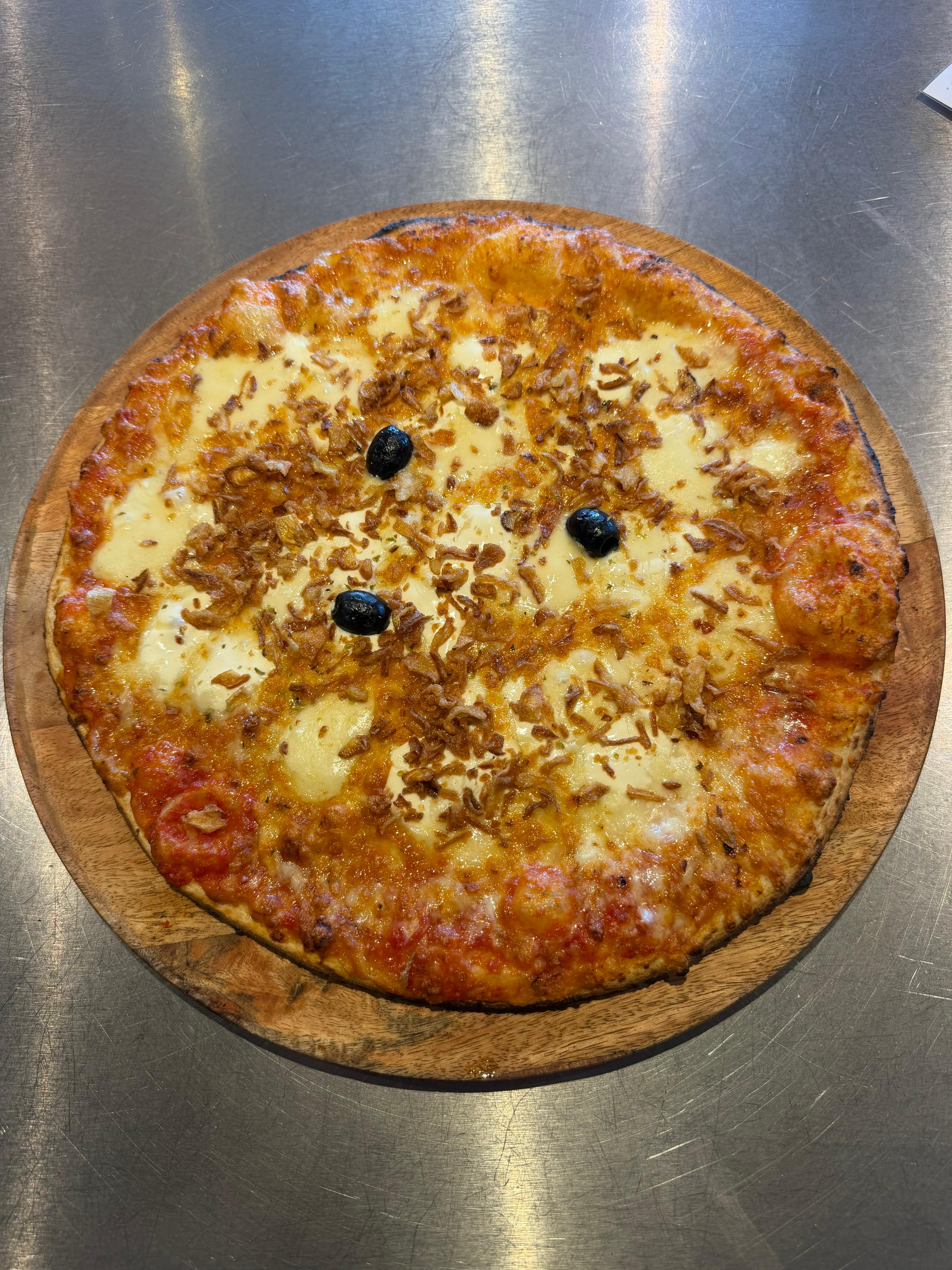 Pizza blanche signature Lou, garnie de mozzarella fraîche fondante, d'un mélange d'emmental, d'une touche de crème et d'olives noires, présentée sur une assiette.