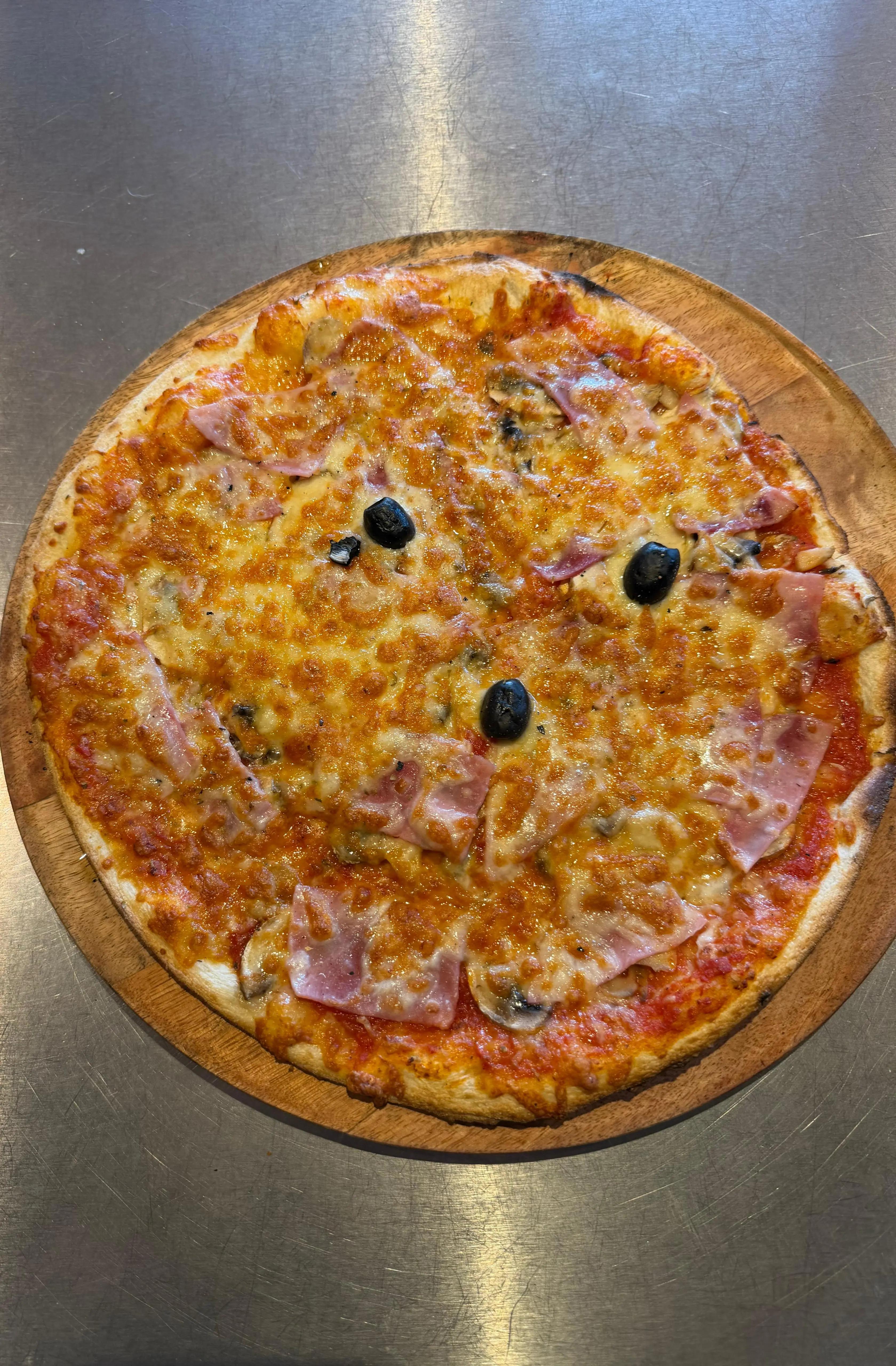 Pizza Regina artisanale garnie de jambon blanc, champignons, fromage fondu et olives noires, présentée sur une planche en bois à la pizzeria Chez Matteo au Porge.