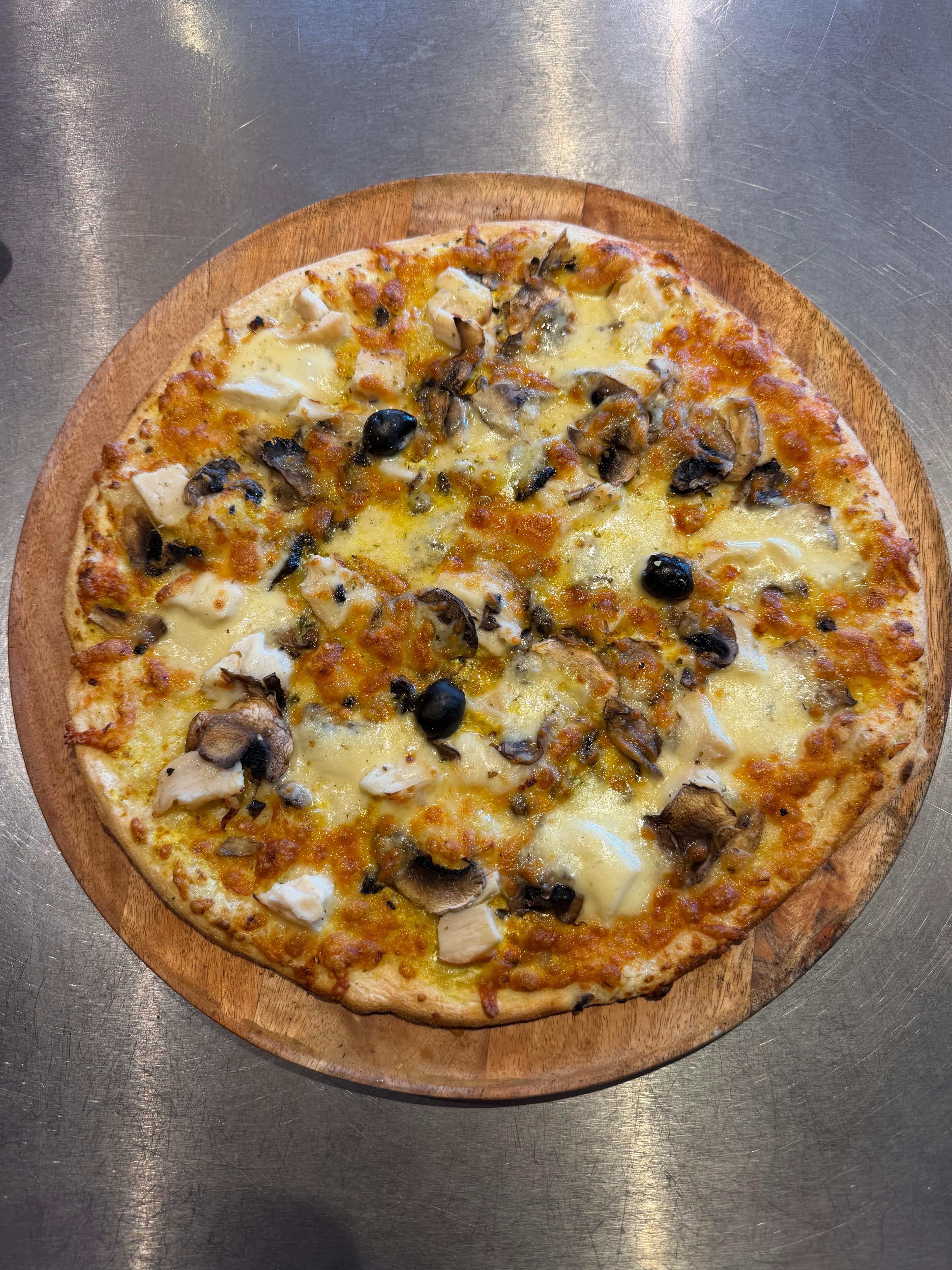 Pizza artisanale généreusement garnie de morceaux de poulet, champignons frais, fromage fondu et olives noires, servie sur une planche en bois à la pizzeria Chez Matteo au Porge.