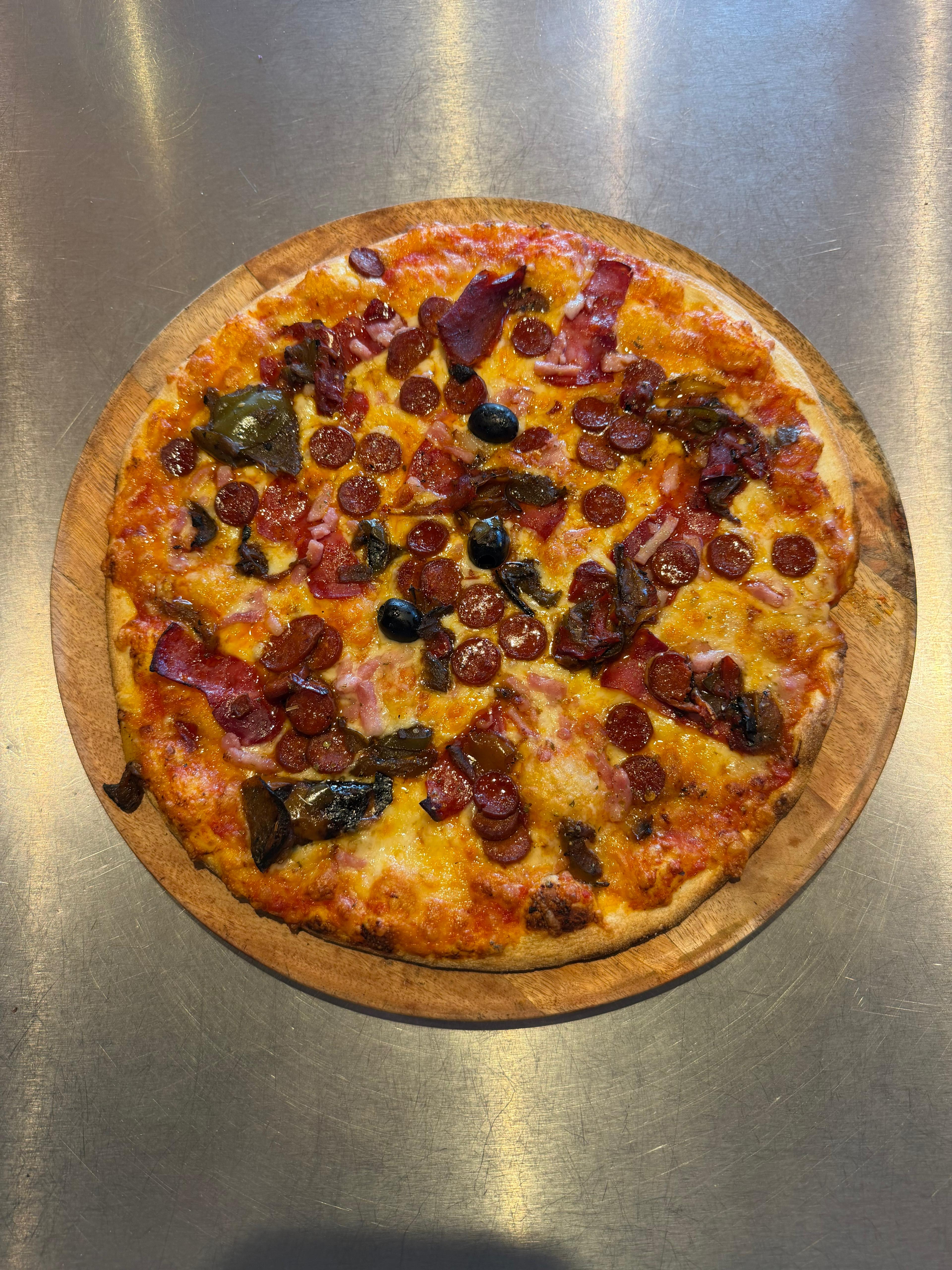Pizza artisanale généreusement garnie de rondelles de chorizo, lardons, poivrons, fromage fondu et olives noires, présentée sur une planche en bois à la pizzeria Chez Matteo au Porge.