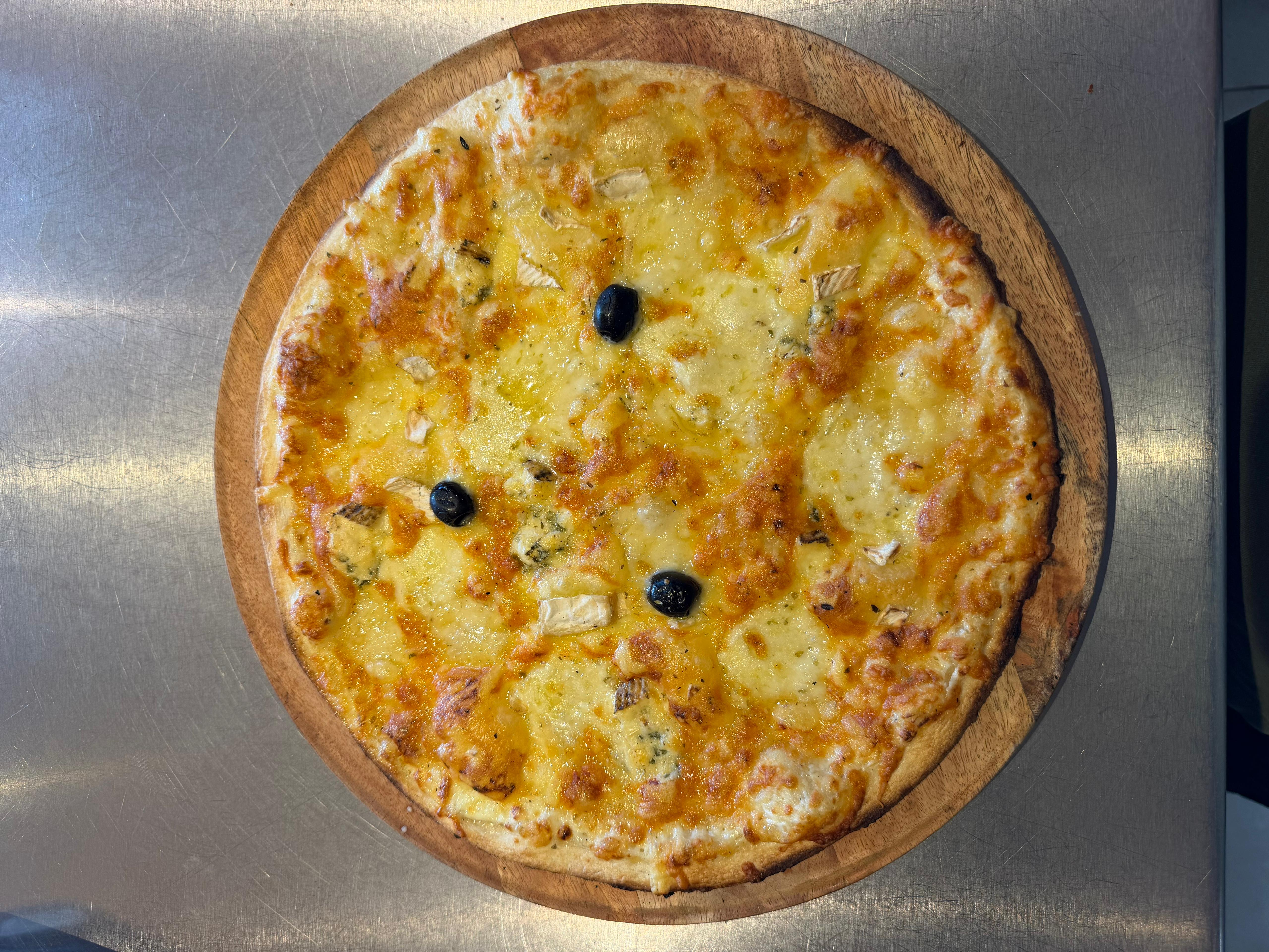 Pizza 7 Fromages artisanale très gourmande, garnie de comté, mozzarella fraîche, bleu, camembert, chèvre, reblochon, mélange d'emmental et olives noires, présentée à la pizzeria Chez Matteo au Porge.