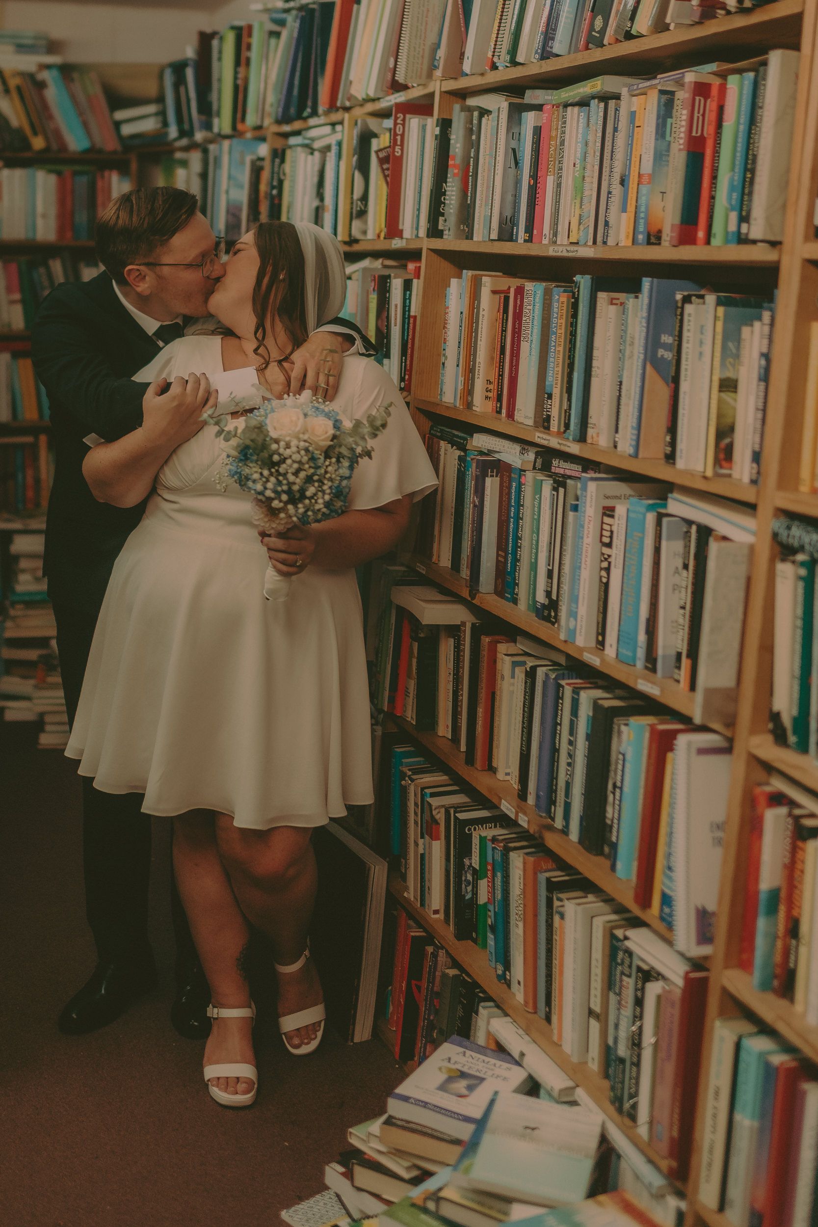 Tiffani and Braden kiss in a narrow bookstore aisle.