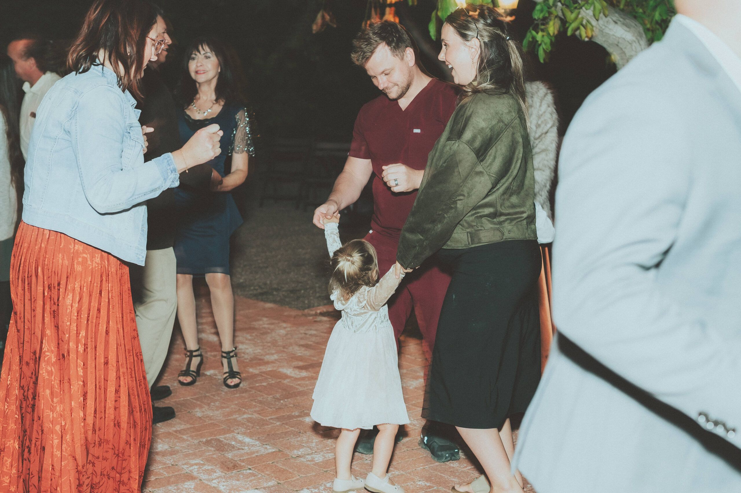 A child dancing with wedding guests during an evening reception.