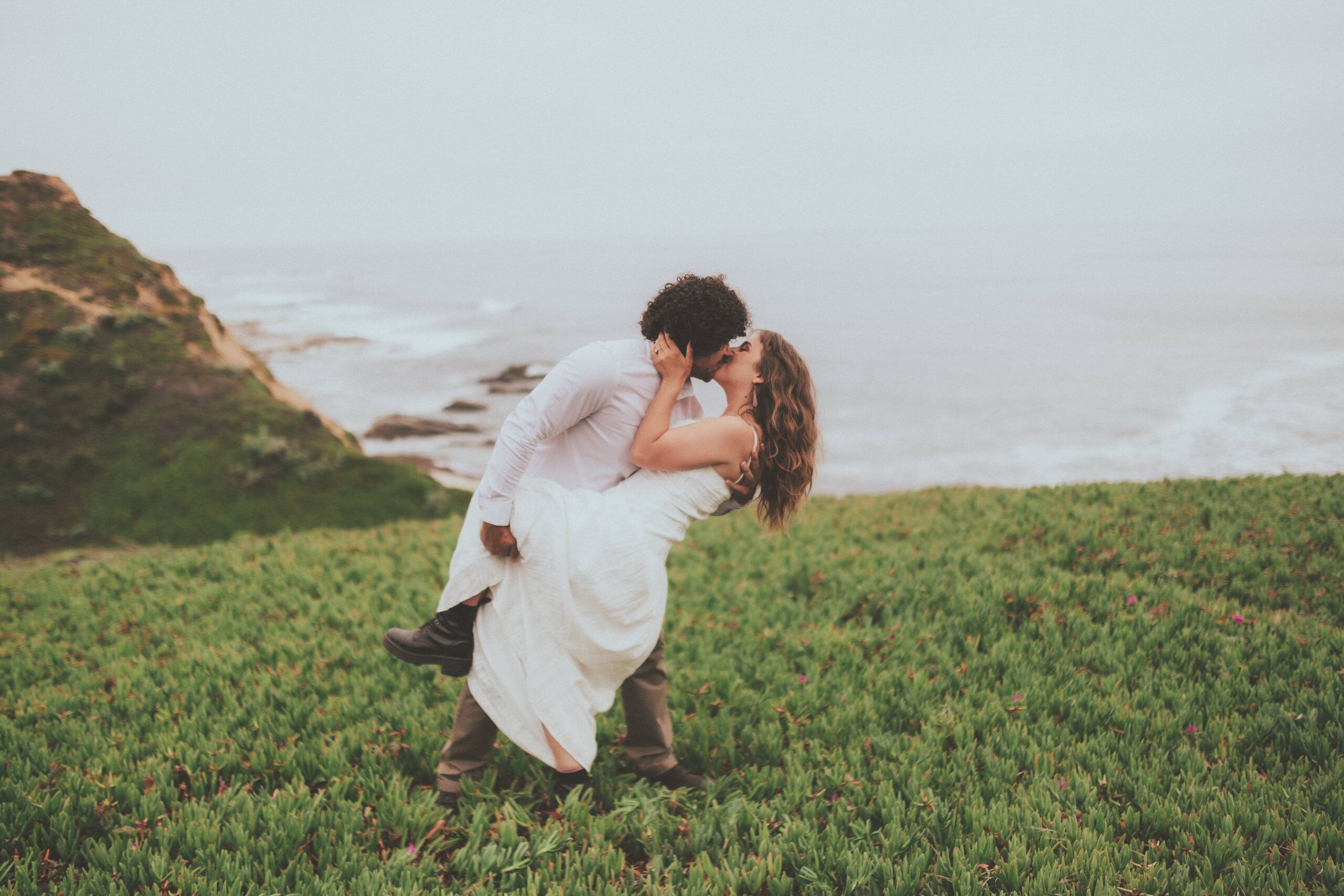 A couple embracing on a green bluff above the ocean.