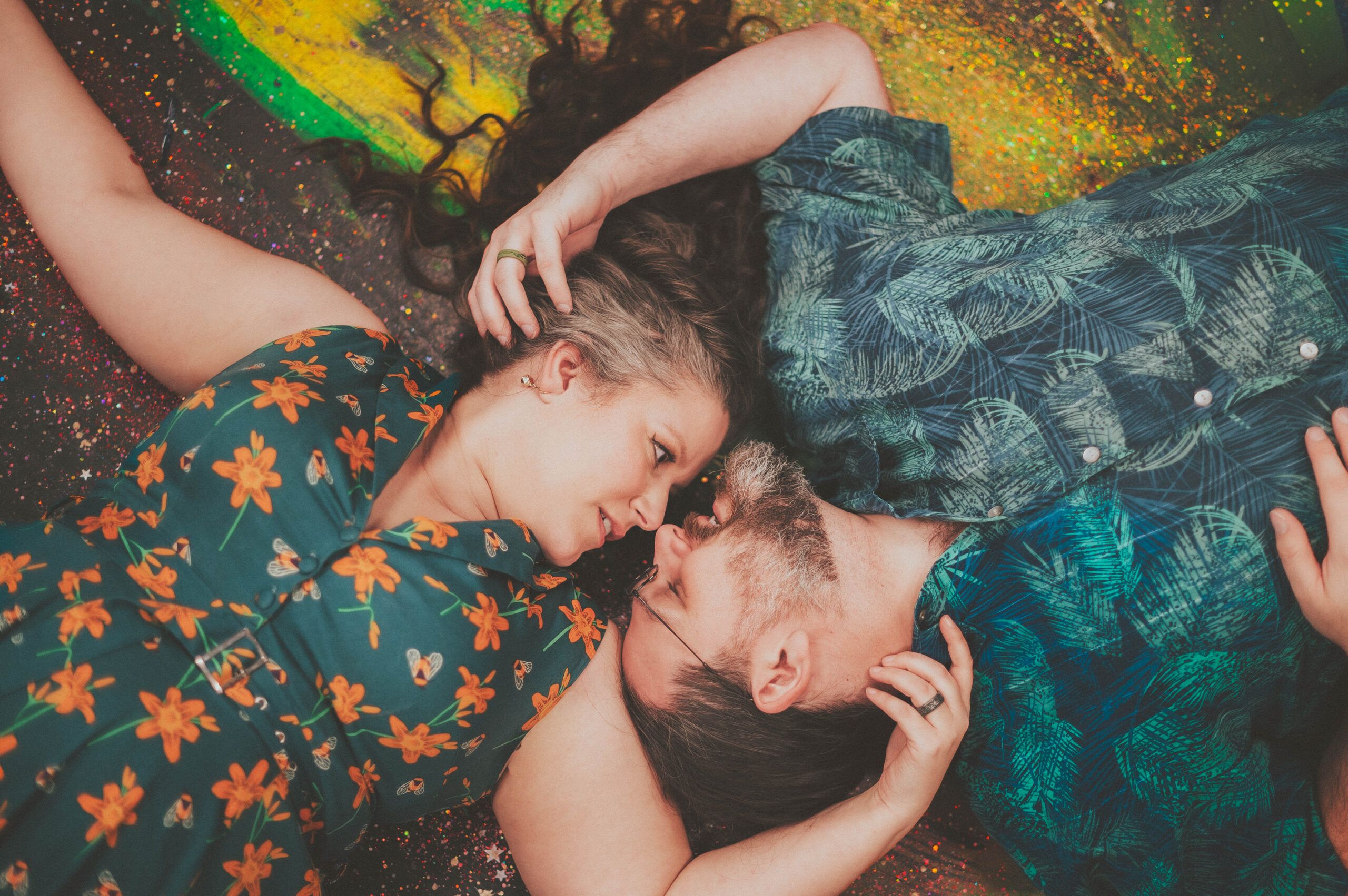 A couple lying close together on a colorful blanket, framed by patterned clothing.