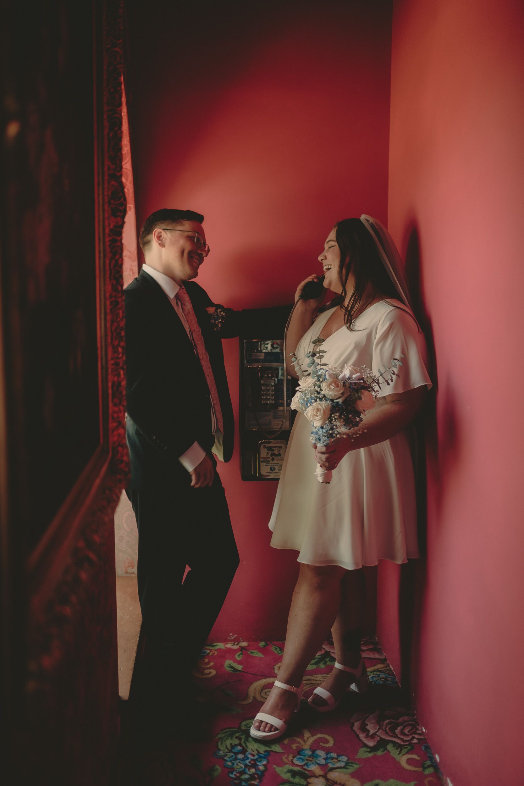 Tiffani and Braden laugh beside a vintage phone in a red room.