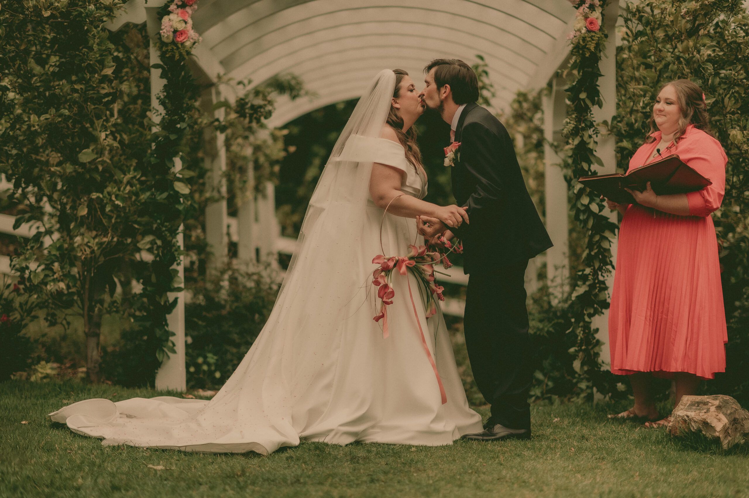 Calla and Bryan kissing beneath a flower-covered garden arch.